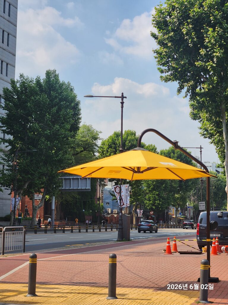 A large automatic crosswalk shade canopy deployed on a Seoul street, representing the innovative pedestrian infrastructure of korea's smart bus stops.